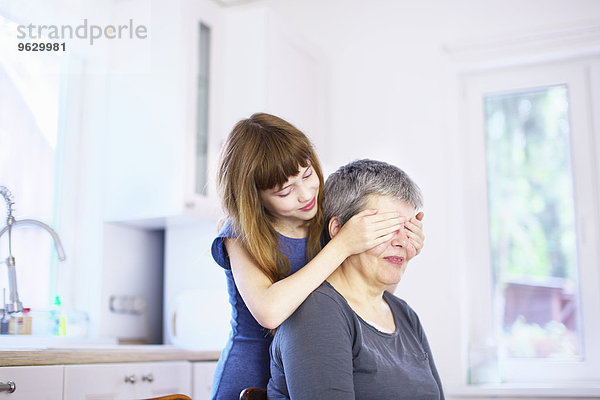 Mädchen  das Großmutters Augen am Küchentisch bedeckt