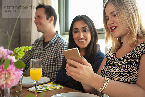 Freunde am Esstisch  junge Frau zeigt Freund Smartphone-Bildschirm