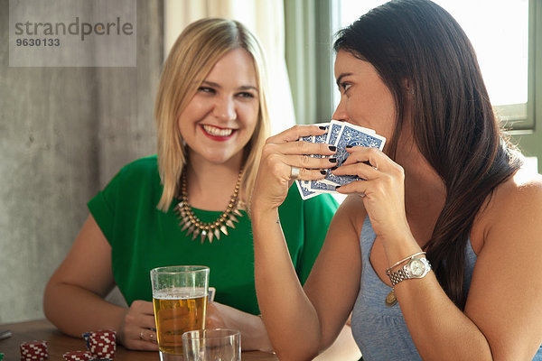 Zwei Freundinnen spielen Karten und lachen am Tisch.