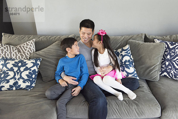 Erwachsener Mann und zwei Kinder sitzen auf dem Wohnzimmersofa