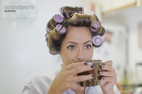 Nahaufnahme einer erwachsenen Frau mit Haarrollen beim Kaffeetrinken