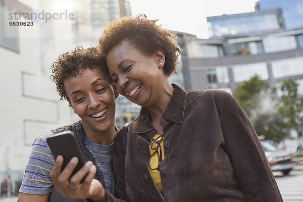 Zwei reife Freundinnen lachen über Smartphone-Texte auf der Straße