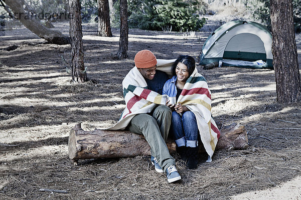 Junges Camping-Paar auf einem Baumstamm sitzend in Decke gehüllt