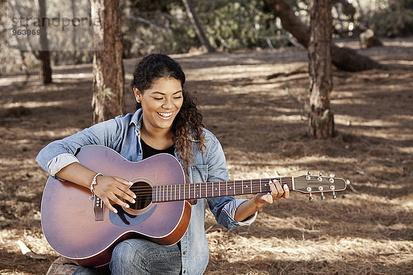 Junge Frau sitzt im Wald und spielt Akustikgitarre