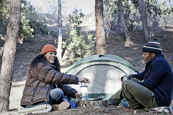 Junges Camping-Paar im Wald sitzend  lachend und plaudernd