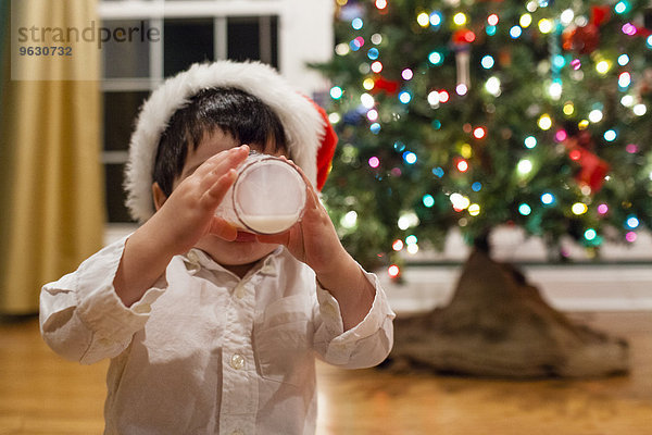 Männliches Kleinkind trinkt Milch vor dem Weihnachtsbaum