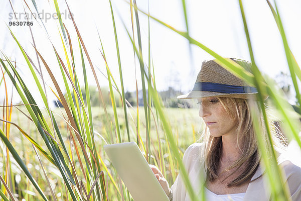 Mittlere erwachsene Frau im langen Gras sitzend  mit digitalem Tablett