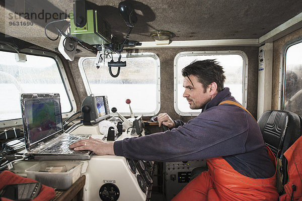 Fischer beim Fahren eines Fischerbootes mit Laptop