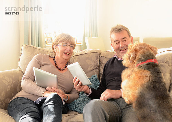 Seniorenpaar zu Hause mit Hund  mit digitalen Tabletten