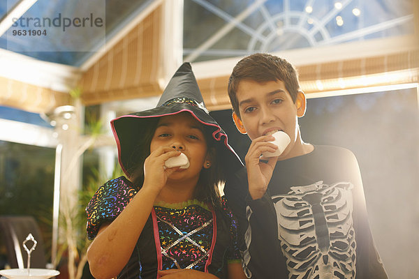 Bruder und Schwester in Halloween-Kostümen essen Marshmallows