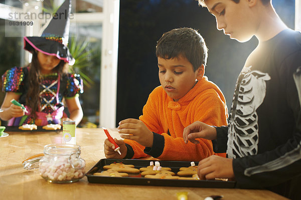 Brüder und Schwestern in Halloween-Kostümen dekorieren Lebkuchenmänner