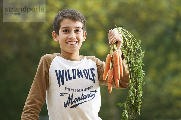 Porträt eines Jungen im Garten  der einen Haufen Karotten hochhält