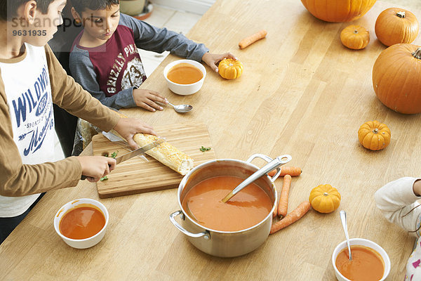 Geschwister bereiten Baguette und Kürbissuppe in der Küche zu.