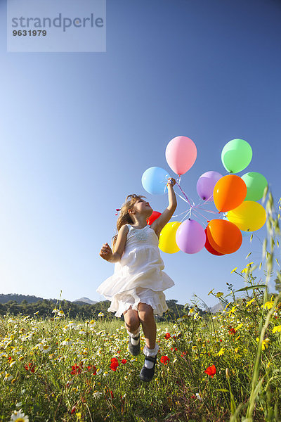Mädchen springen vor Freude mit bunten Luftballons auf der Wildblumenwiese  Mallorca  Spanien