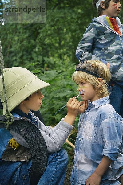 Drei Jungen  die sich im Wald mit Gesichtsbemalung verkleiden.