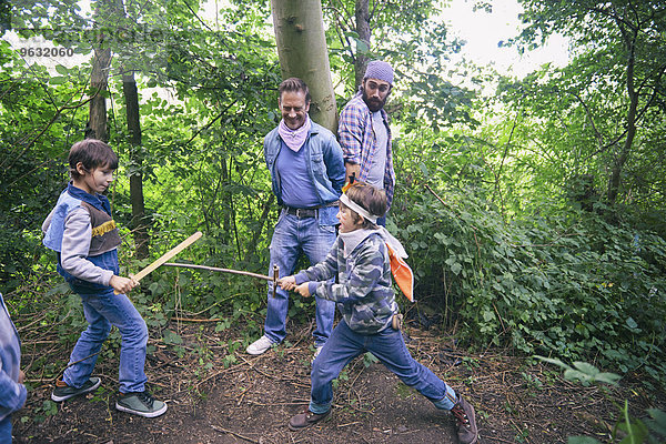 Zwei Männer gefangen  während Jungen im Wald Schwertkampf haben.