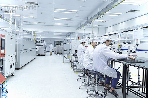 Mitarbeiter mit Mikroskopen in einer Fabrik  die sich auf die Herstellung von Funktionsschaltungen auf flexiblen Oberflächen spezialisiert hat.