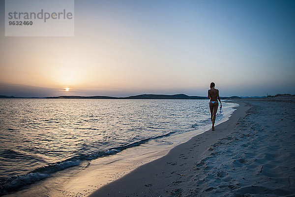 Rückansicht einer jungen Frau  die am Strand spazieren geht und Bikini-Top trägt  Cagliari  Sardinien  Italien