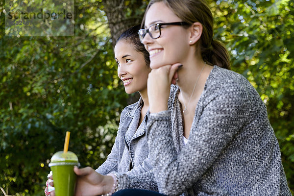 Zwei junge Frauen mit Kaffee zum Mitnehmen sitzend im Park