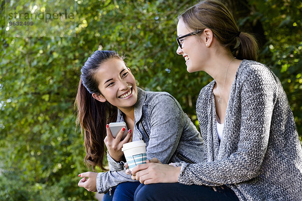Zwei junge Frauen mit Kaffee zum Mitnehmen beim Plaudern im Park
