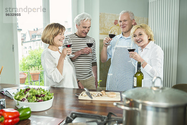 Four senior friends kitchen cooking drinking wine