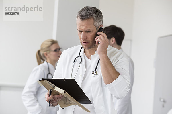 Doctor on phone with file while colleagues in background