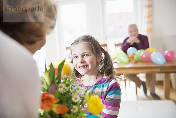 Granddaughter hand over bunch of flowers to her grandmother while grandfather in background