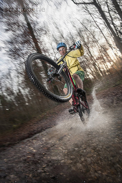 Mountain Biker rides on the rear wheel through a stream in the forest