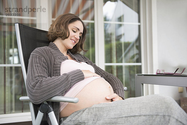 Woman pregnant sitting terrace holding stomach