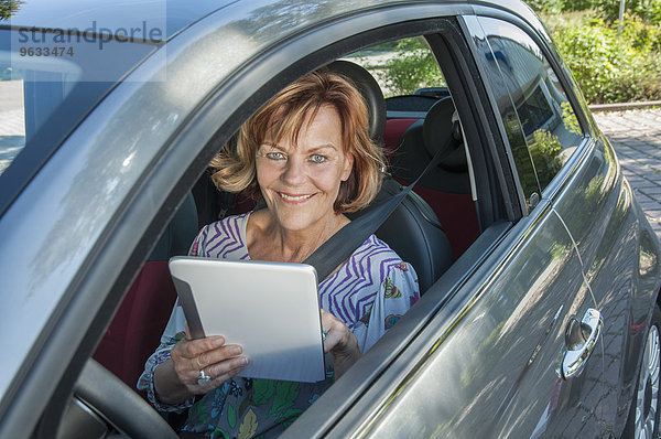 Senior woman sitting in car and using digital tablet