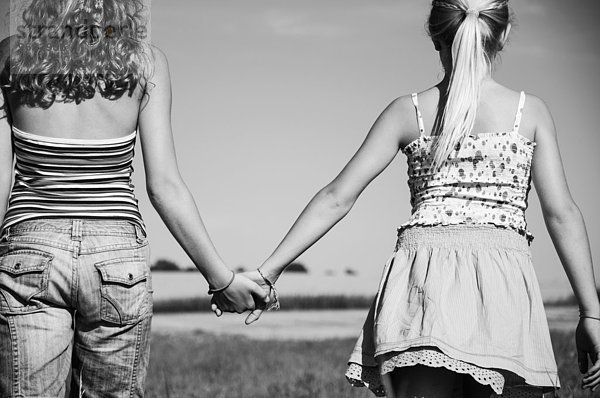 Two girls (10-11) (12-13) hand in hand in field  rear view