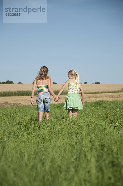 Two girls (10-11) (12-13) hand in hand in field  rear view