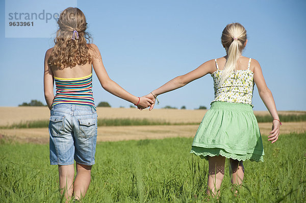 Two girls (10-11) (12-13) hand in hand in field  rear view