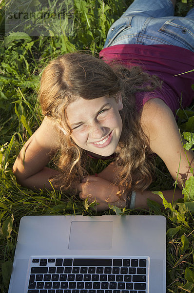 Girl (12-13) in meadow using laptop  elevated view