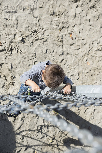 Small boy playground climbing chain from above