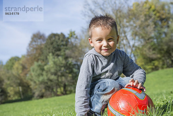 Portrait small boy red football meadow smiling