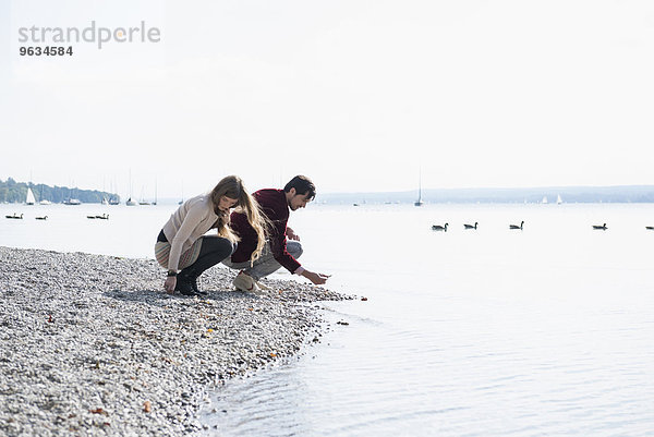 Young couple lake shore gathering pebbles