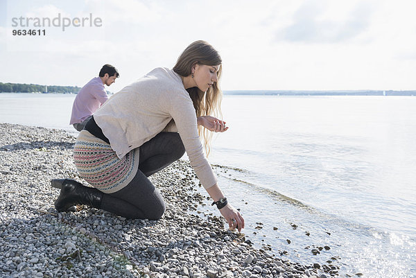 Young couple lake shore gathering pebbles