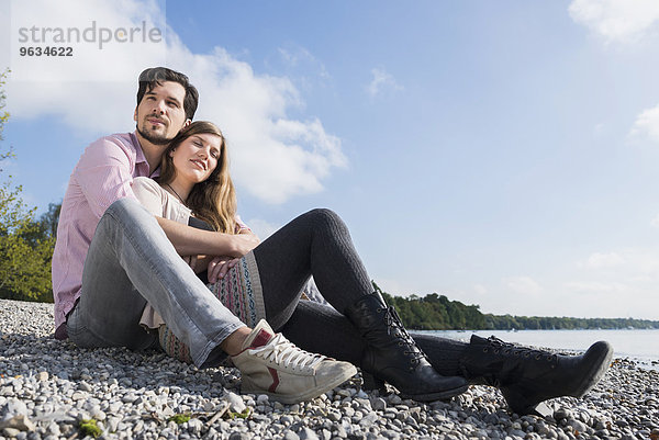 Couple sitting hugging lake shore happy