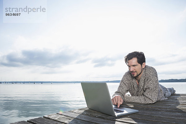 Man outdoors lake working laptop computer