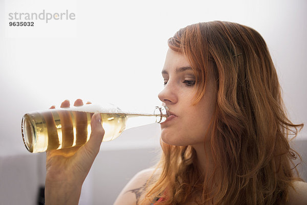 Young red-haired woman drinking beer from the bottle