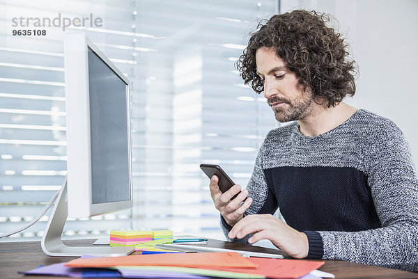 Businessman working on computer and text messaging on mobile phone