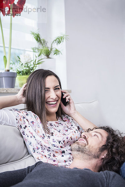 Woman talking on mobile phone with her husband lying on lap