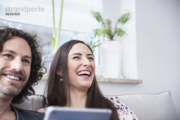 Couple laughing on couch with using digital tablet