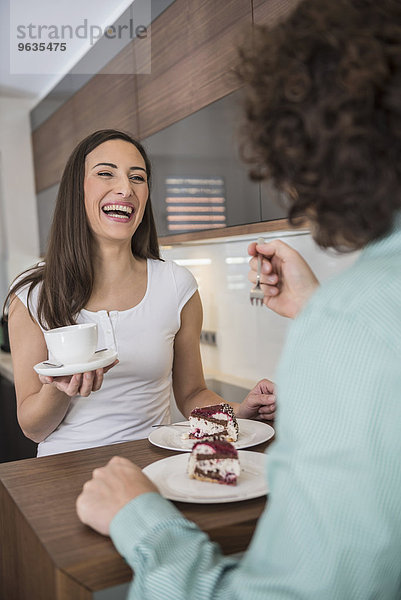 Couple eating slice of cake in a kitchen and laughing