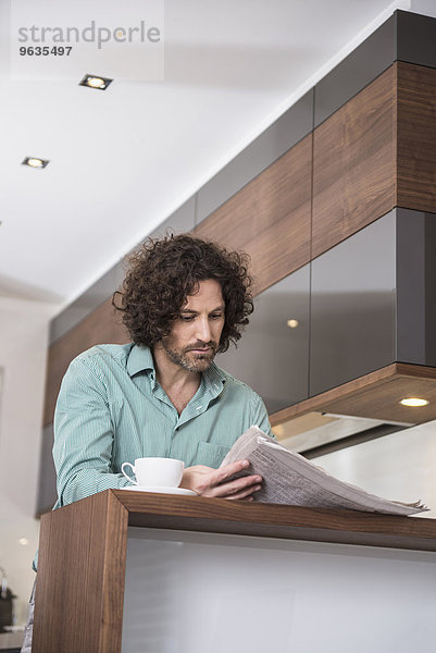 Man sitting in a kitchen and reading a newspaper