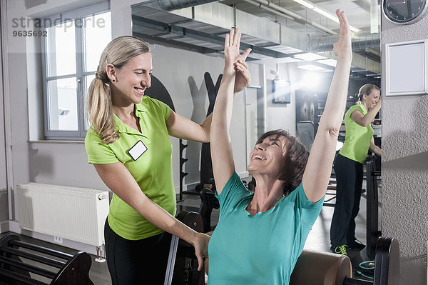 Fitness trainer helping mature woman stretching