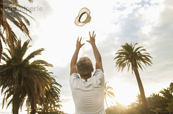 Teenager boy throwing hat in air palm trees happy