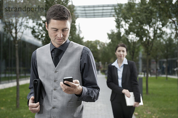Businessman reading message on a mobile phone with his partner in the background