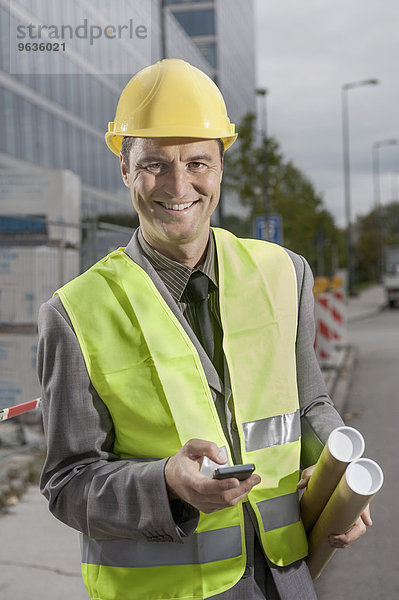 Portrait of a happy site manager holding blueprints and mobile